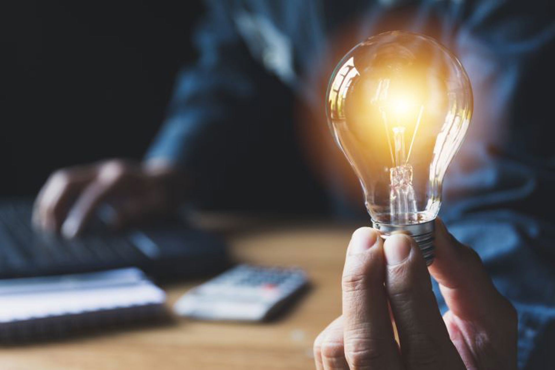 Hand holding lightbulb with laptop